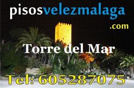 Anuncio de pisos en Vélez-Málaga con una torre iluminada y número de teléfono al pie.