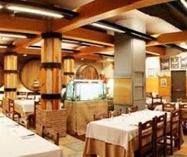 Restaurante acogedor con mesas vestidas y decoración de madera y barriles en las paredes.