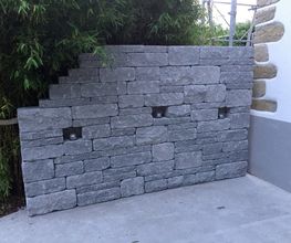 Graue Ziegelmauer mit abgestufter Kante, eingebettetem Licht, steht vor Bambus und Wand.