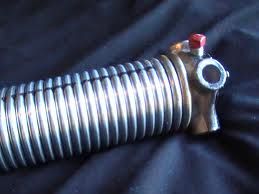 Close-up of a metal coil with a red valve against a dark fabric background.