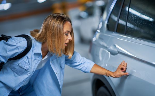 Frau prüft, ob im Lack des Autos ein Kratzer ist.