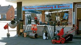 Geschäft für Werkzeugvermietung mit verschiedenen Geräten vor dem Laden, darunter eine Rüttelplatte.