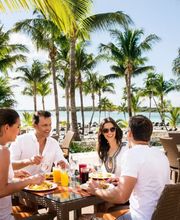 Grupo de personas comiendo al aire libre en un restaurante tropical junto a la playa.