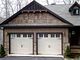 A rustic-style house with two beige garage doors and stone accents, set in a wooded area.