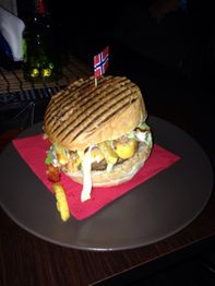 Hamburger con patatine e bandierina norvegese su un tovagliolo rosso in un piatto grigio.