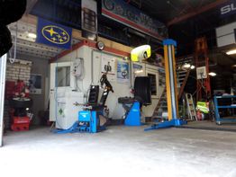 Autogarage-interieur met gereedschap, hefbrug en banden tegen de muur.