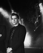 Due uomini in posa davanti a un murale illuminato in bianco e nero sullo sfondo.