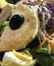 Salat mit geröstetem Brot, Käse, schwarzen Oliven, Eiern und buntem Gemüse auf einem Teller.