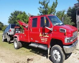Red tow truck towing a silver SUV on a grassy path under a clear blue sky.