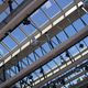 Glazen dak met metalen balken en spots, zicht op blauwe hemel.