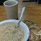 Bowl of porridge with a spoon, cup of coffee, and swirled rye bread on a wooden table.