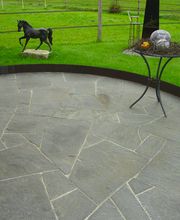 Steinplatte Terrasse mit Tisch, Deko-Stein, Hufeisen und Skulptur eines Pferdes im Hintergrund.