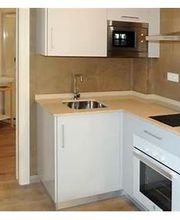 Cocina moderna en tonos neutros con microondas, horno, lavadora y baño al fondo.