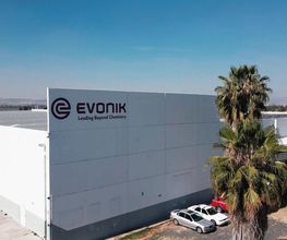 Edificio de Evonik con palmera y coches estacionados bajo un cielo despejado.