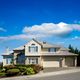 Suburban house with a well-kept garden under a bright blue sky with clouds.