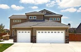 Modern house with beige exterior, two garages, and a sloped roof under a partly cloudy sky.