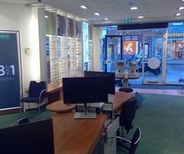 Optiekwinkelinterieur met stoelen, display met brillen en een bureau met computers.