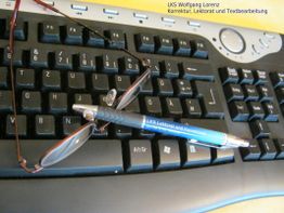 Brille und Stift auf schwarzer Tastatur, im Hintergrund ein gelber Bildschirmrand.