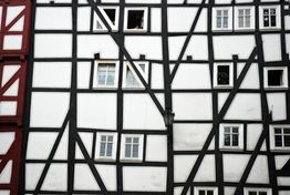 Fachwerkhausfassade mit weißen Wänden und dunklen Balken, mehrere Fenster unregelmäßig verteilt.