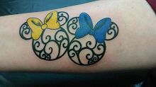 Tattoo of two mouse heads with swirls and bows, one yellow and one blue, on an arm.