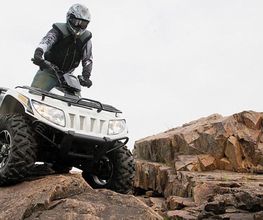 Persona conduciendo un quad sobre rocas en un día nublado.