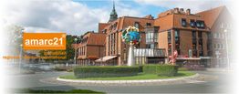 Gebäudeensemble mit rundem Platz, Kunstskulptur und amarc21 Immobilien-Logo links.