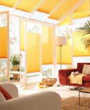 Helles Wohnzimmer mit gelben Jalousien, rotem Sofa, Pflanzen und Sonnenlicht.