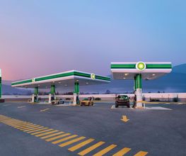 Estación de servicio con dos autos cargando combustible al atardecer.