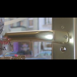 Nahaufnahme eines silbernen Türgriffs an einer Glastür, im Hintergrund unscharf eine Straße.