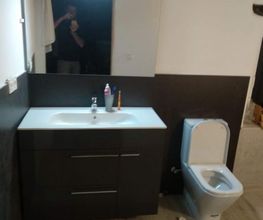 Baño moderno con lavabo, espejo, inodoro y reflejo de persona tomando la foto visible en el espejo.