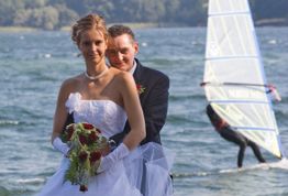 Ein Brautpaar am See, hinten ein Windsurfer.