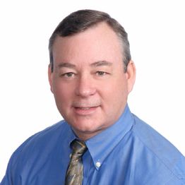 Man in blue shirt and tie smiling at the camera against a white background.