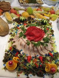 Platte mit dekorativ angerichtetem Fleisch, Obst und Gemüse, umgeben von Salat und grünem Dekor.