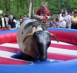 Ein Kind reitet auf einem mechanischen Bullen, umgeben von Zuschauern im Freien.