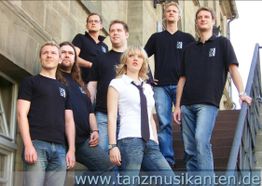 Gruppe von sieben Personen in Freizeitkleidung posiert auf einer Treppe vor einem Gebäude.