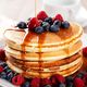 Stack of pancakes with syrup, blueberries, and raspberries on a white plate.