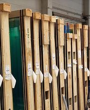 Große Glasplatten in Holzrahmen stehen in einer Lagerhalle nebeneinander aufgereiht.