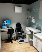 Kleine optometrieruimte met stoel, bureau, computer en oogmeetapparatuur.