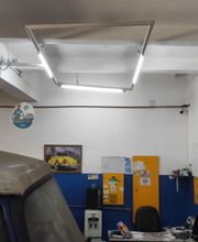 Oficina com painel azul e amarelo, carro coberto à esquerda e quadro de carro na parede.