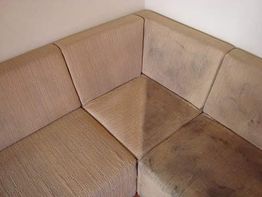 Sofá de canto em tecido bege com manchas escuras nas almofadas.