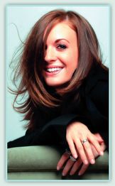 Junge Frau mit braunen Haaren lächelt in die Kamera, stützt sich auf grünes Sofa.