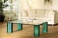 Wohnzimmer mit weißem Sofa und Glastisch mit grünen Beinen, Pflanzen in der Ecke.