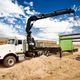 Truck-mounted crane lifting a green structure on a construction site under a blue sky.