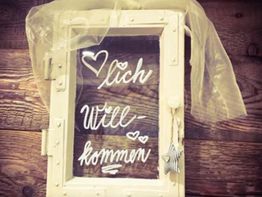 Willkommensschild mit handgeschriebenem "Herzlich Willkommen" und Herzdekorationen auf Holz.