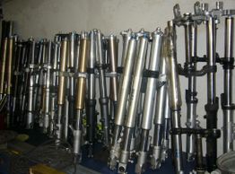 Mehrere Motorradgabeln in verschiedenen Farben stehen dicht nebeneinander an einer Wand.