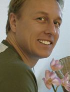 Eine lächelnde Person in einem grünen Oberteil neben rosa Blume.