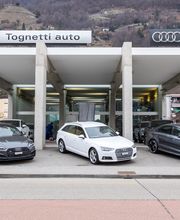 Autohaus mit drei Audi-Modellen vor modernen Gebäuden und Bergkulisse.