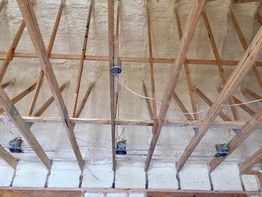 Wooden ceiling beams with light fixtures and spray foam insulation on the roof.