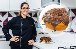 Cozinheira ao lado de um bolo decorado com cobertura de chocolate e granulado na cozinha.