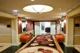 Hotel hallway with red sofas, patterned carpet, overhead lighting, and exit sign.